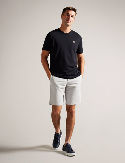 A man standing in a casual pose wearing knee-length light grey shorts and a dark navy t-shirt, with belt loops and pockets visible on the shorts.
