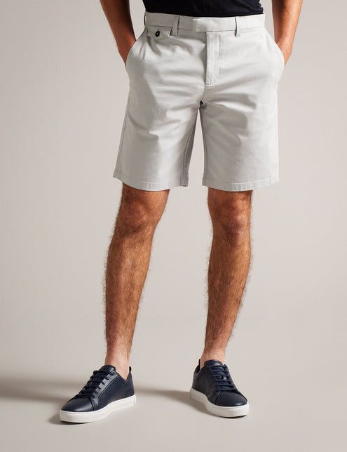 A man standing in a casual pose wearing knee-length light grey shorts and a dark navy t-shirt, with belt loops and pockets visible on the shorts.