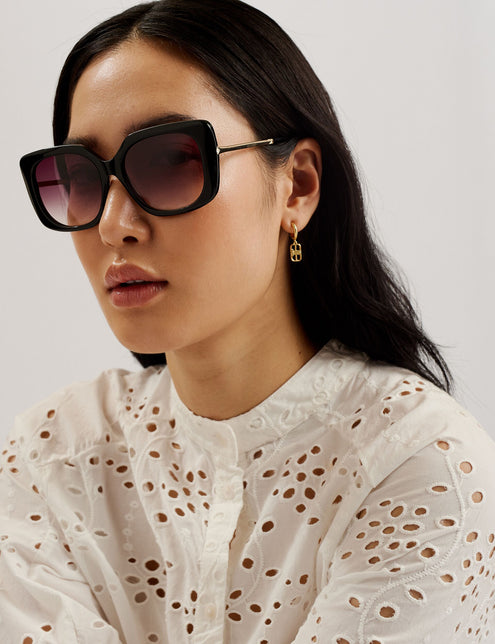 A woman wearing a white midi dress with broderie anglaise design, featuring an oversized fit, puff half sleeves, and a half button placket with a grandad collar.