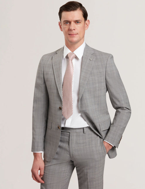 A male model wearing a light grey suit jacket with a notched lapel, single-breasted two-button fastening, and flap front pockets. He is also wearing a white shirt and a patterned tie.
